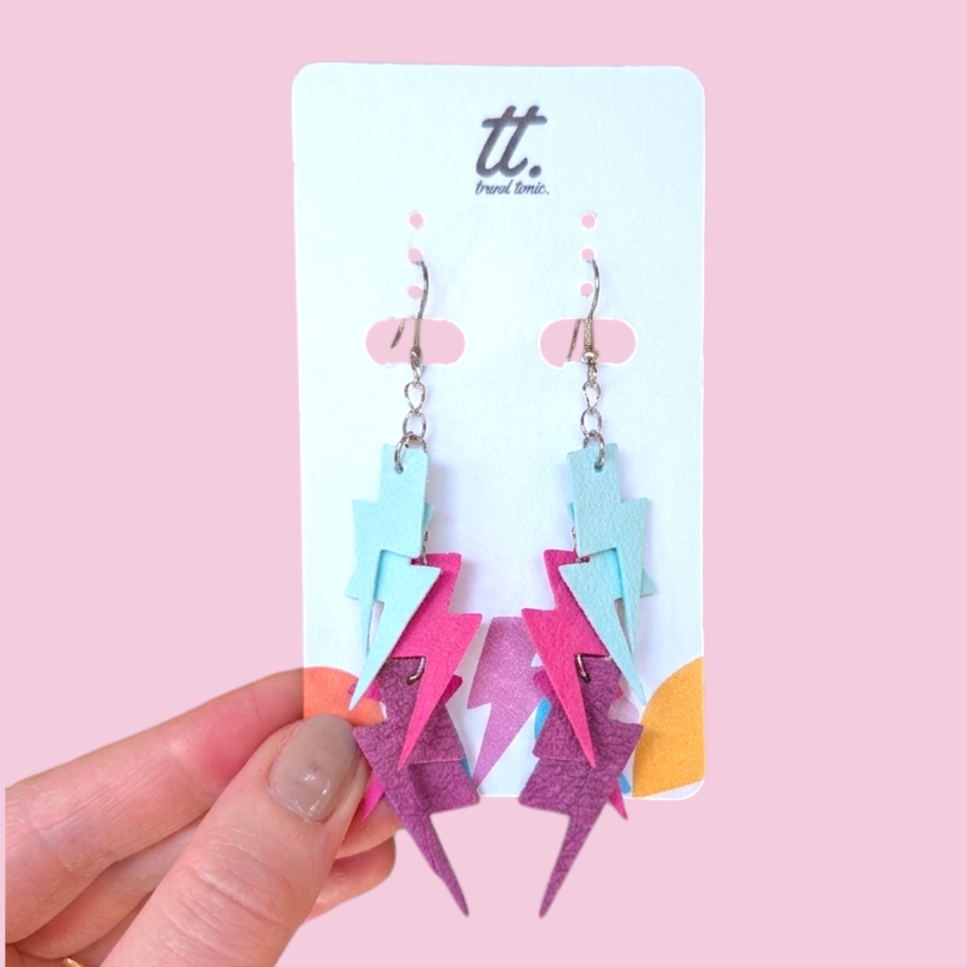 a hand holding a pair of lightning bolts earrings