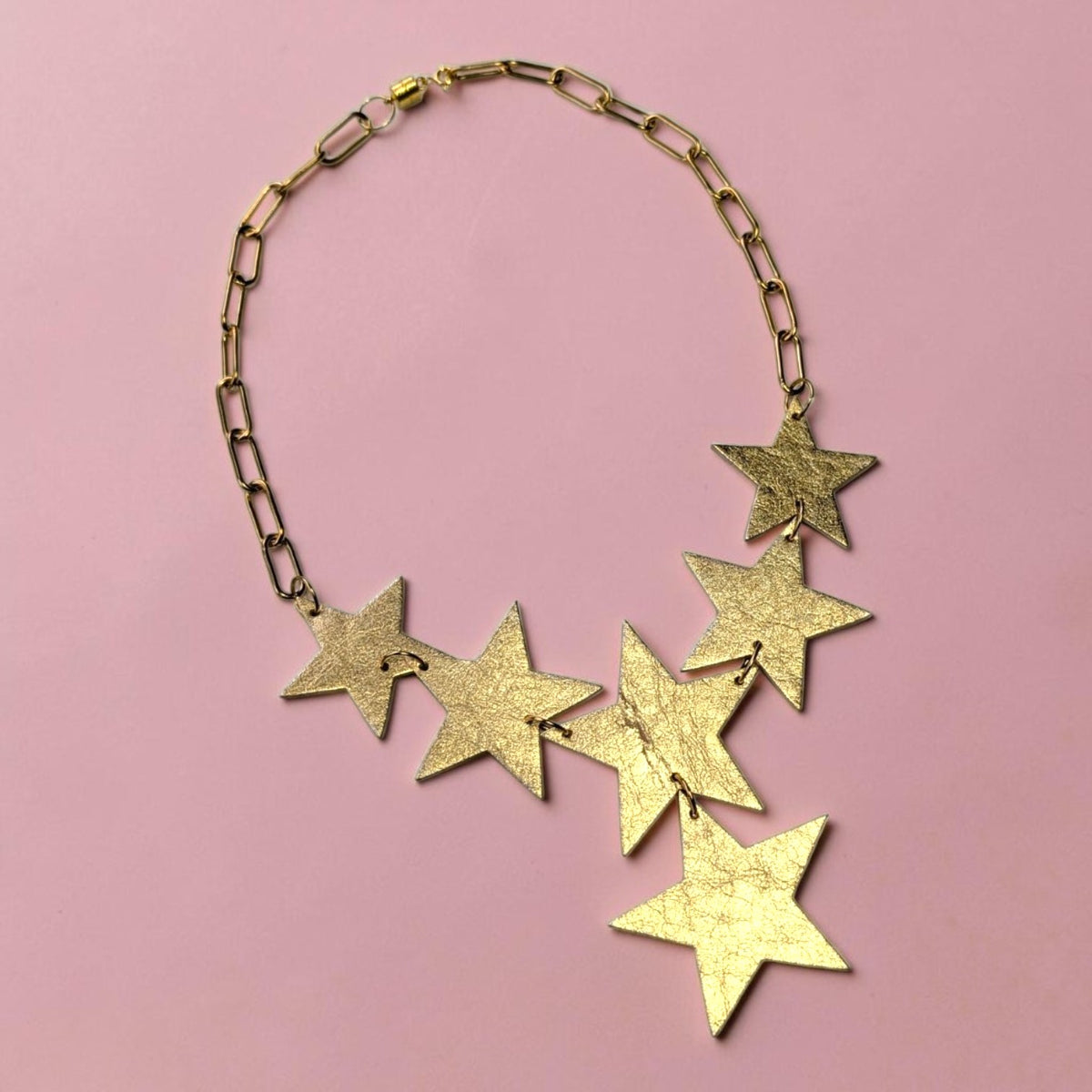a gold star necklace on a pink background