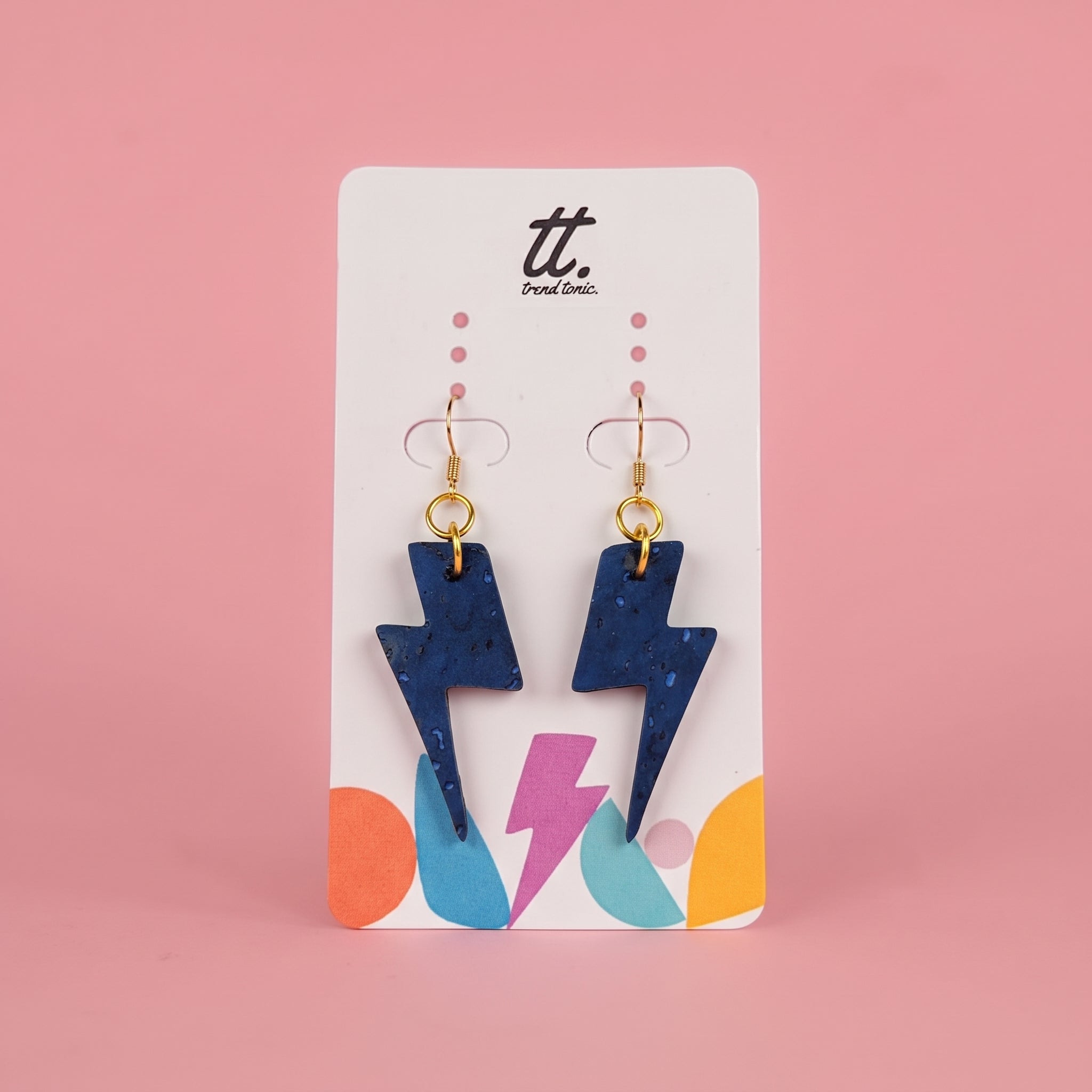A pair of blue lightning bolt drop earrings with gold hooks, displayed on a white card with colorful abstract shapes and the brand name 'tt. Port City.