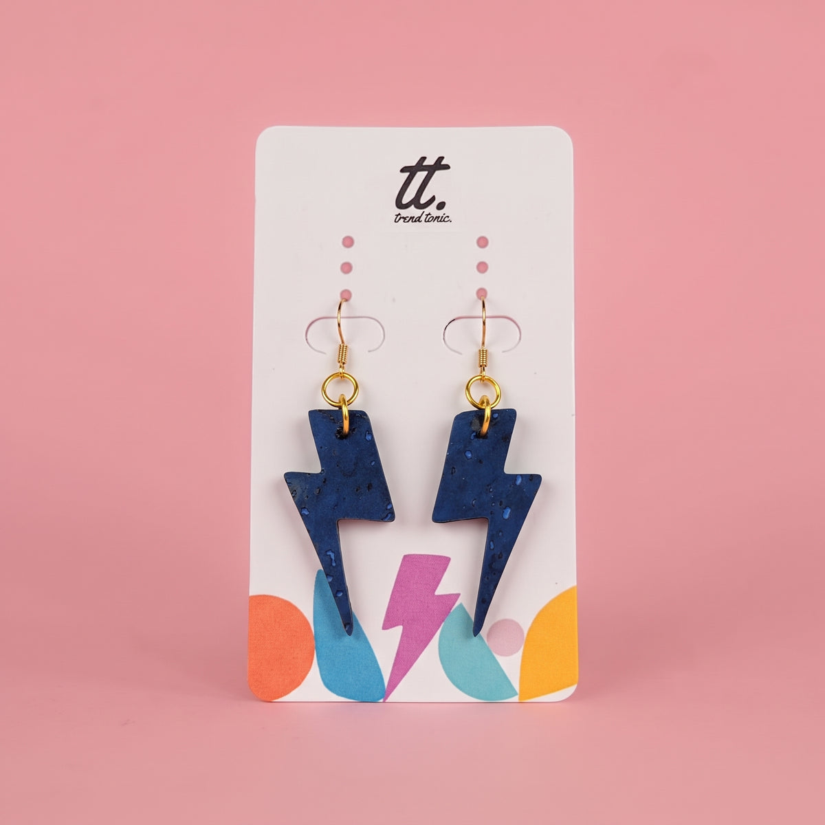 A pair of blue lightning bolt drop earrings with gold hooks, displayed on a white card with colorful abstract shapes and the brand name 'tt. Port City.