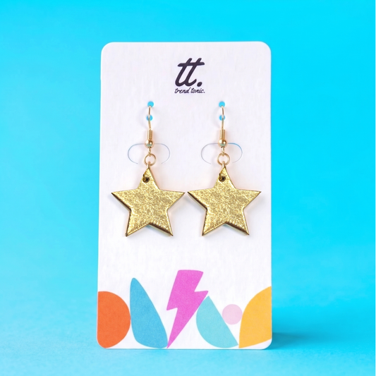 a pair of gold star earrings on a white card