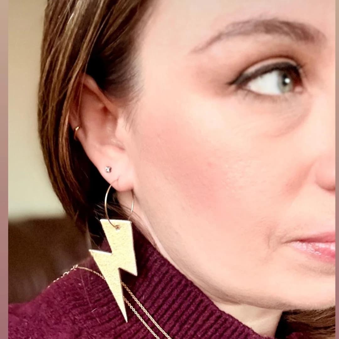 a woman wearing a gold lightning bolt earring