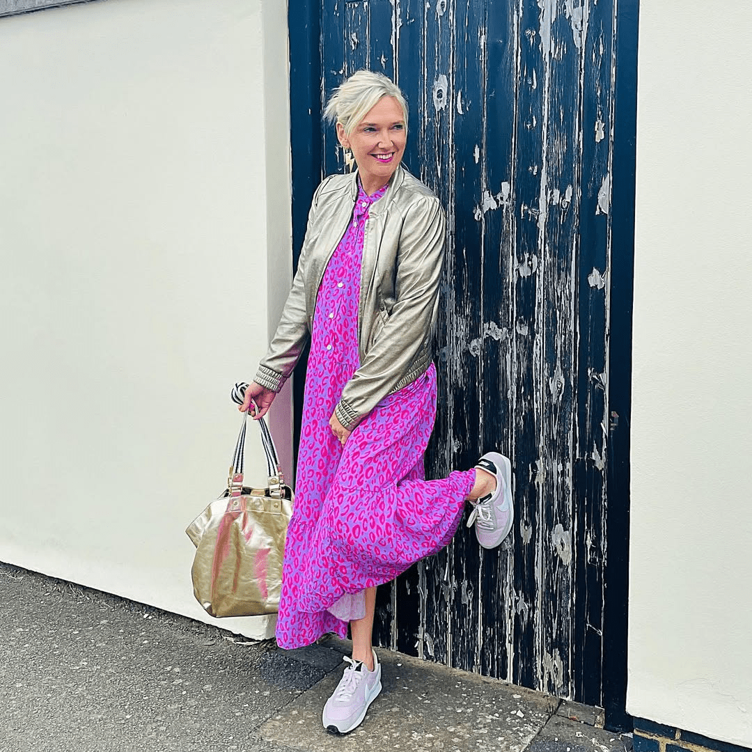 a woman in pink dress and silver jacket leaning against a door