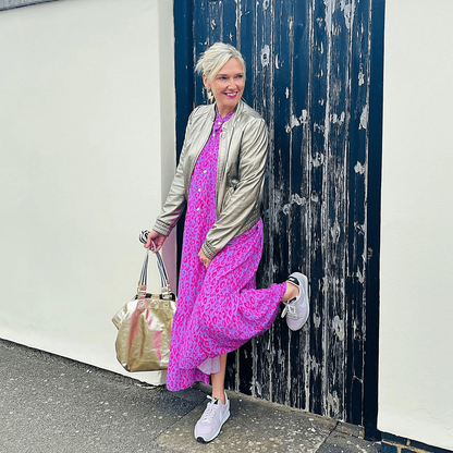 a woman in pink dress and silver jacket leaning against a door