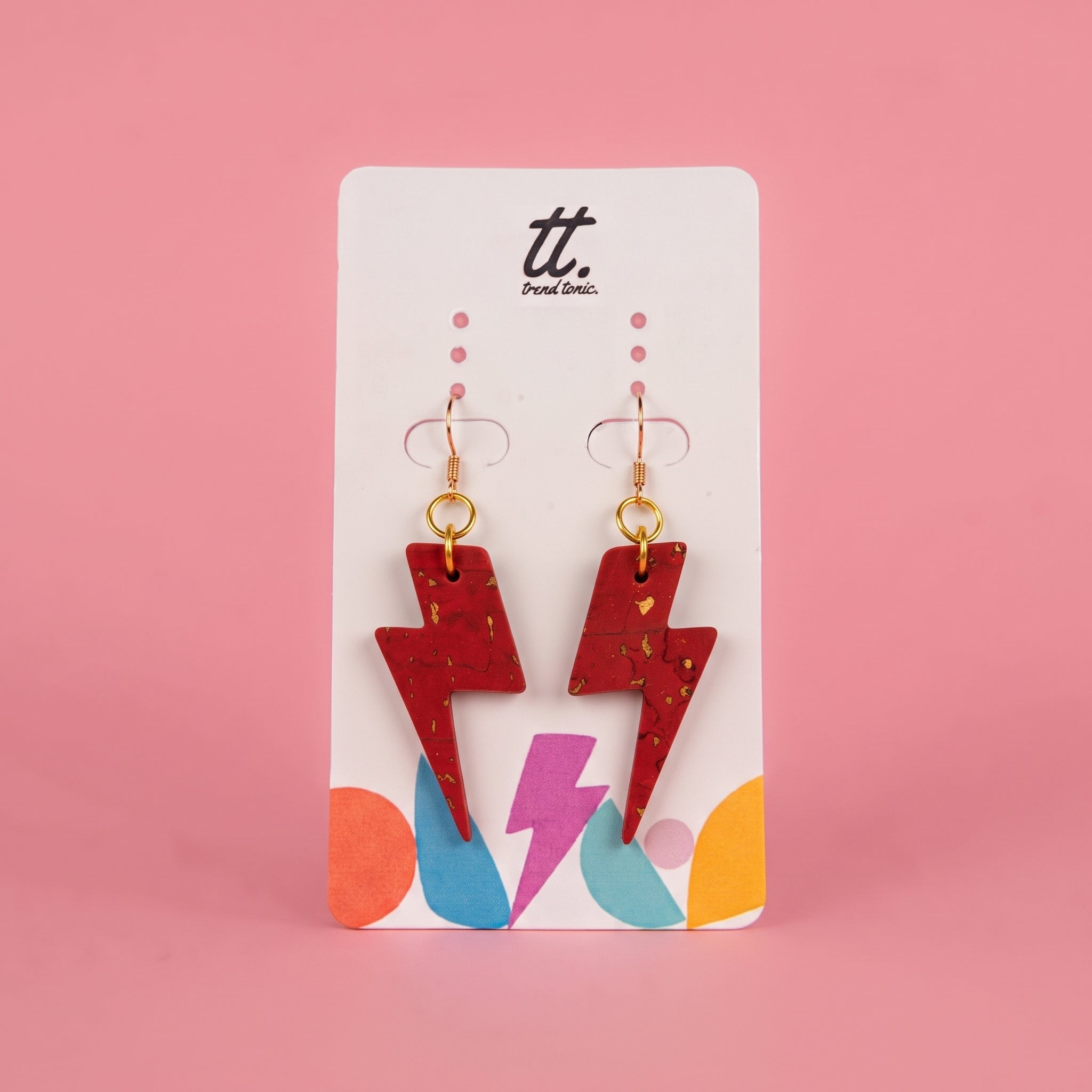 A pair of red lightning bolt drop earrings and gold hooks, displayed on a white card with the 'tt. Punk Clio.