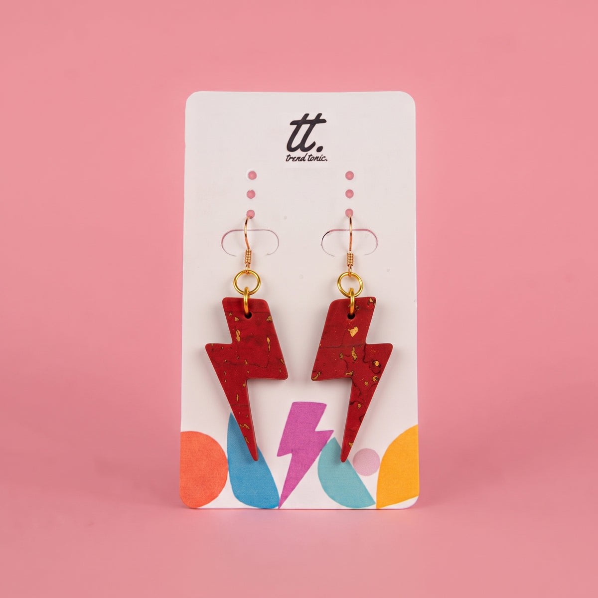 A pair of red lightning bolt drop earrings and gold hooks, displayed on a white card with the 'tt. Punk Clio.
