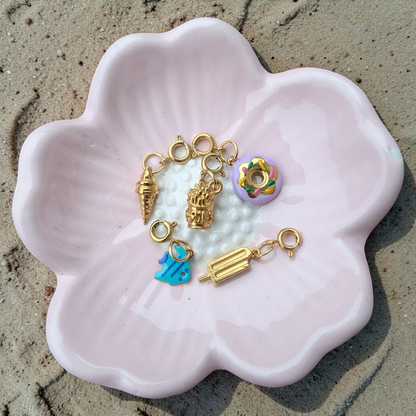 a pink flower shaped dish with gold charms and a donut